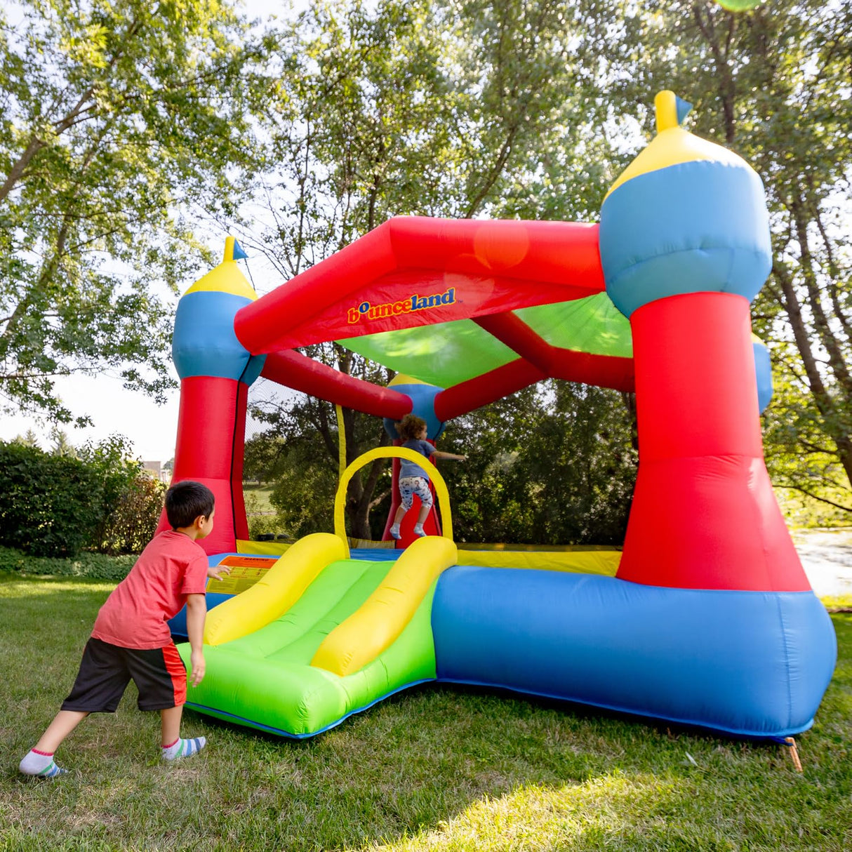 Bounceland Inflatable Party Castle Bounce House Bouncer, 16 ft L x 13 ft W x 10.3 ft H, Basketball Hoop, Removable Sun Roof, UL Strong Blower included, Fun Slide and Bounce Area, Castle Theme for Kids Bounceland